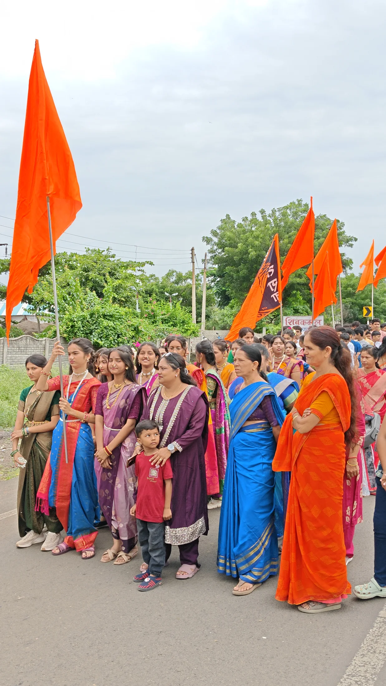 Women and students standing with saffron flags during Ganpati arrival