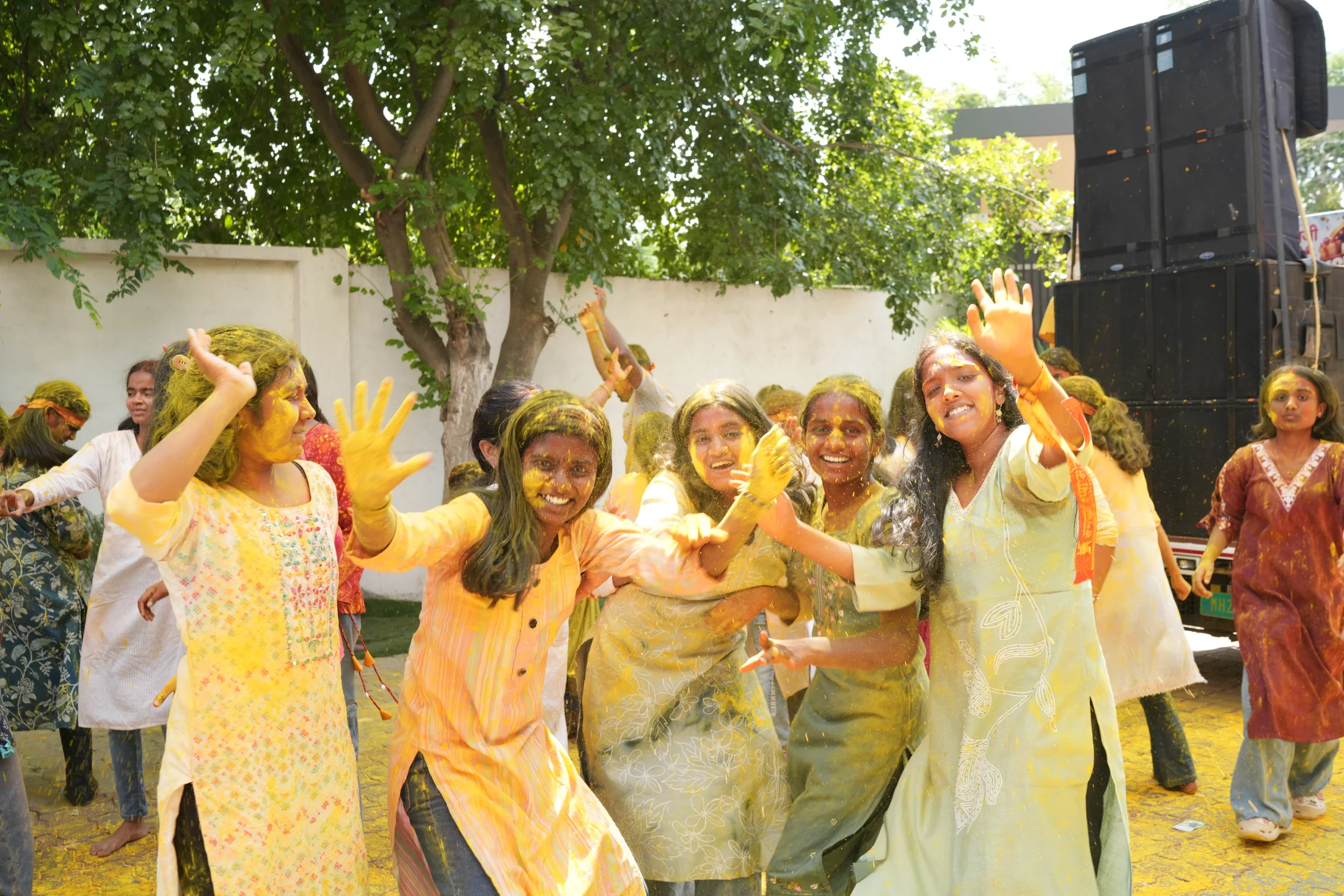 Students celebrating with music, dance, and gulal on the campus lawn